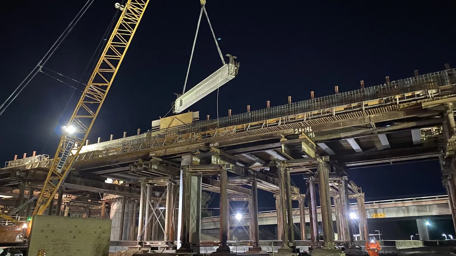 Night construction on a California High-Speed Rail viaduct, with a crane lifting a concrete girder